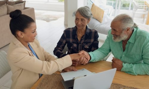 Front view of African-American man shaking hands with financial adviser while sitting beside wife indoor. Authentic Senior Retired Life Concept
